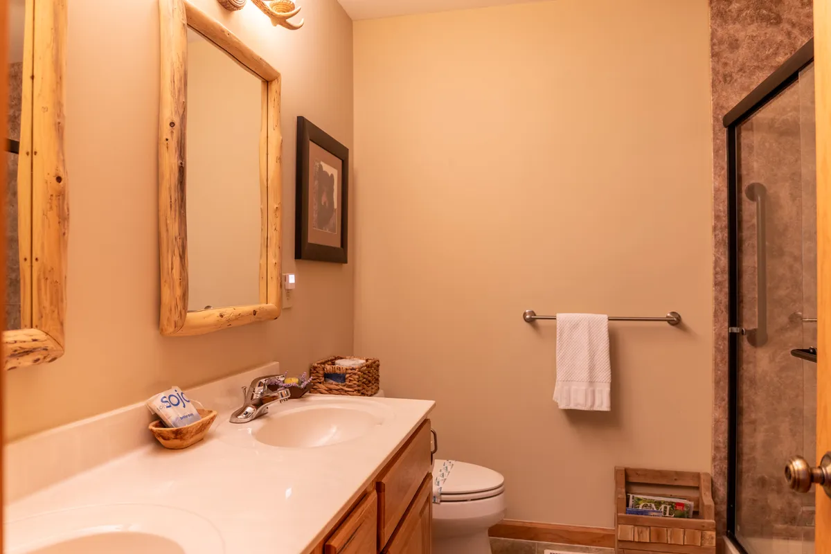 A bathroom featuring double sinks with mirrors, wooden accents, and a shower area. The calming palette and open layout make it ideal for relaxing self-care routines after a day of adventure.