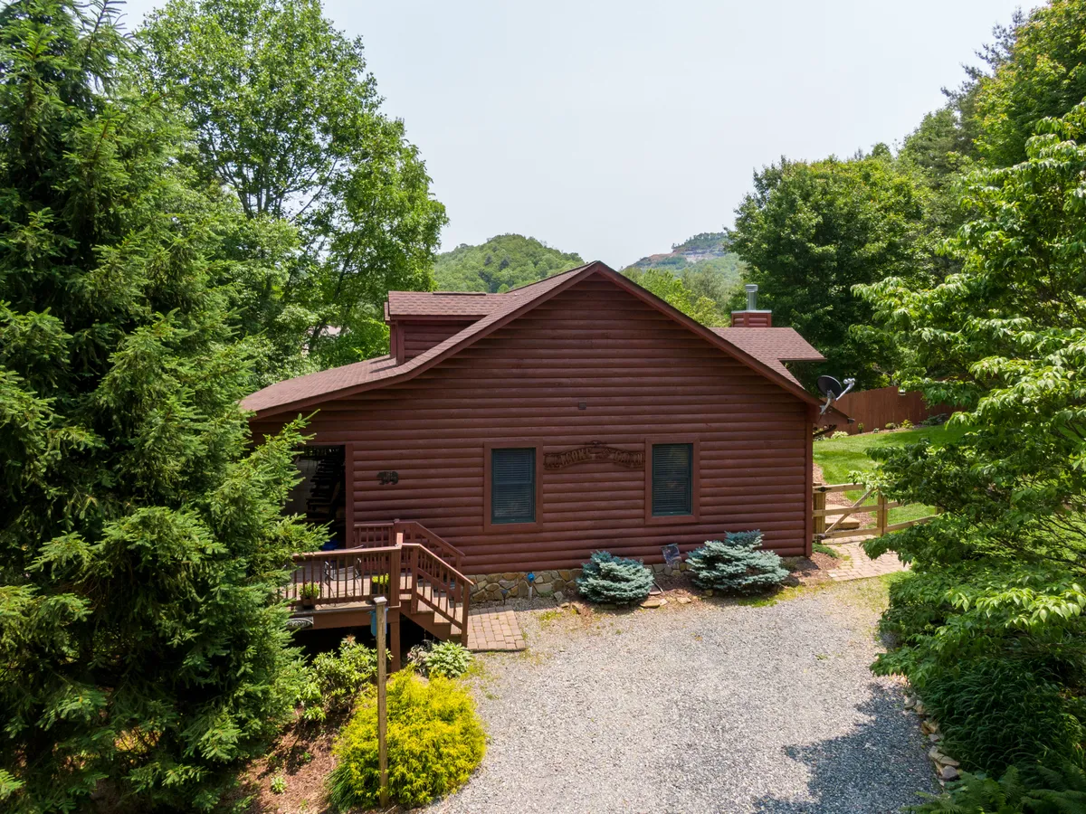 This image showcases the log cabin structure of Bear N Grace nestled amidst lush greenery, with a spacious front porch that hints at a welcoming outdoor environment. The scene exudes a family-friendly atmosphere, perfect for gatherings and outdoor play.