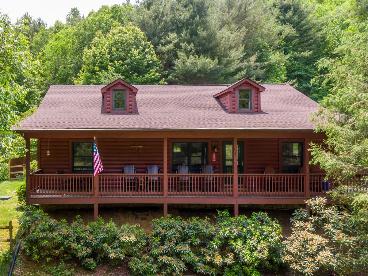 The image shows the front porch of Bear N Grace, adorned with wooden accents, an American flag, and surrounded by greenery. The inviting porch suggests a place for social gatherings, morning coffee, or enjoying sunset views. The open and convivial atmosphere invites guests to relax, mingle, and take in the fresh mountain air right at the threshold between indoor comfort and outdoor adventure.