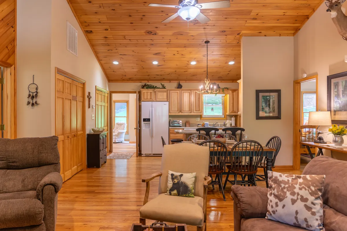 This image features a bright interior space with a wooden ceiling, a spacious dining area, comfortable seating, and decorative wall items. The room feels open and inviting, with natural light highlighting the communal table and the cozy ambiance. The space suggests flexibility for both work and relaxation, making it ideal for remote work or casual gatherings.