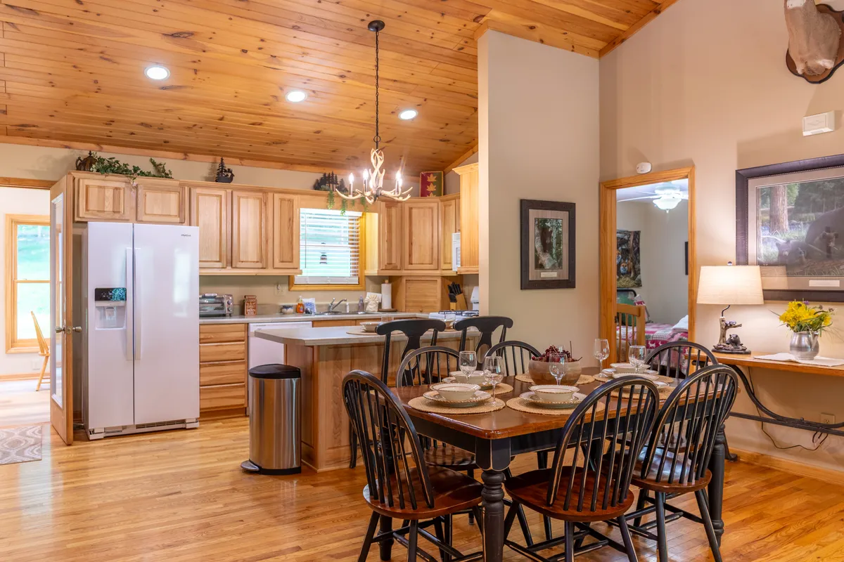 The image showcases a bright dining area set for a meal, with wooden cabinets and an open kitchen layout visible in the background. The design is warm and inviting, perfect for cooking, dining, and entertaining guests.