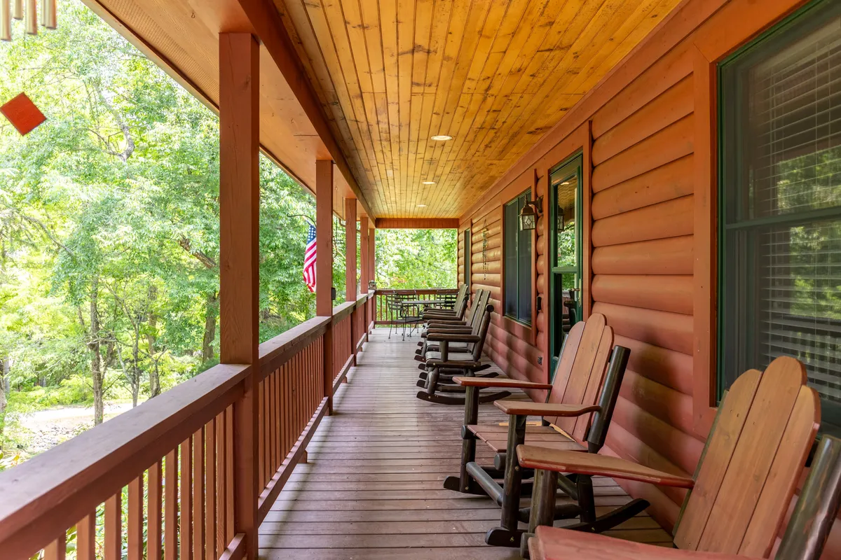 This image highlights a porch area with classic rocking chairs facing out toward lush greenery and an American flag, framed by a wooden railing. The space is ideal for relaxing outdoors, enjoying a book, sipping coffee, or socializing with friends while taking in the natural surroundings.