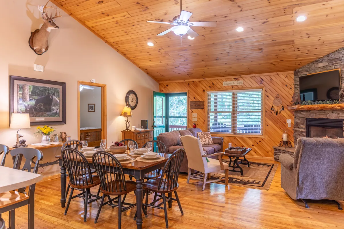 A welcoming open-plan area featuring a dining table with set place settings, comfortable seating area, natural wood accents, and decorative wall art. The layout encourages group meals, conversation, and relaxation, with the living and dining spaces seamlessly connected.